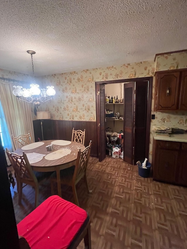dining space with wainscoting, wallpapered walls, a textured ceiling, and a chandelier