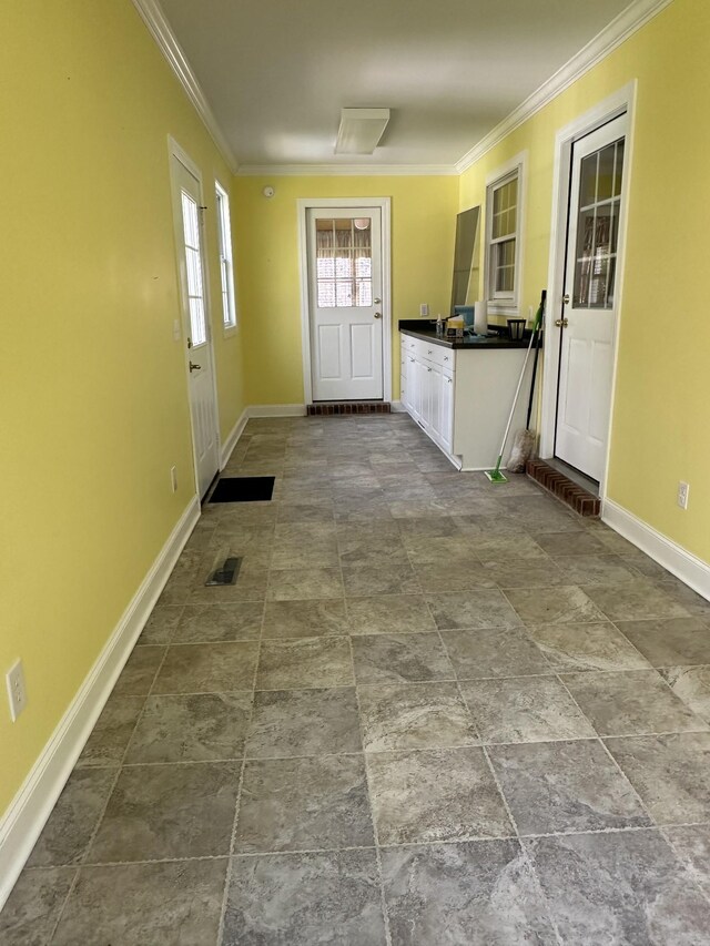 doorway with baseboards, crown molding, stone finish floor, and visible vents