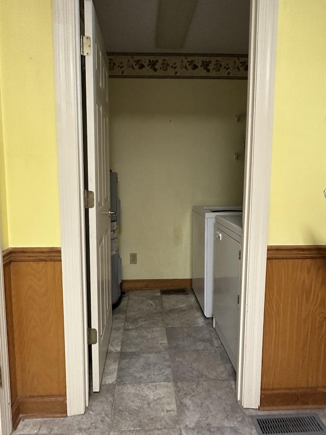 clothes washing area featuring visible vents, water heater, stone finish flooring, washer and dryer, and laundry area