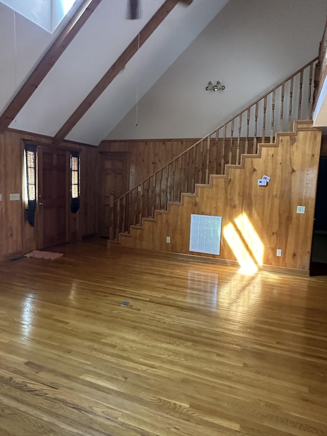 unfurnished living room with wooden walls, stairway, beam ceiling, and hardwood / wood-style flooring