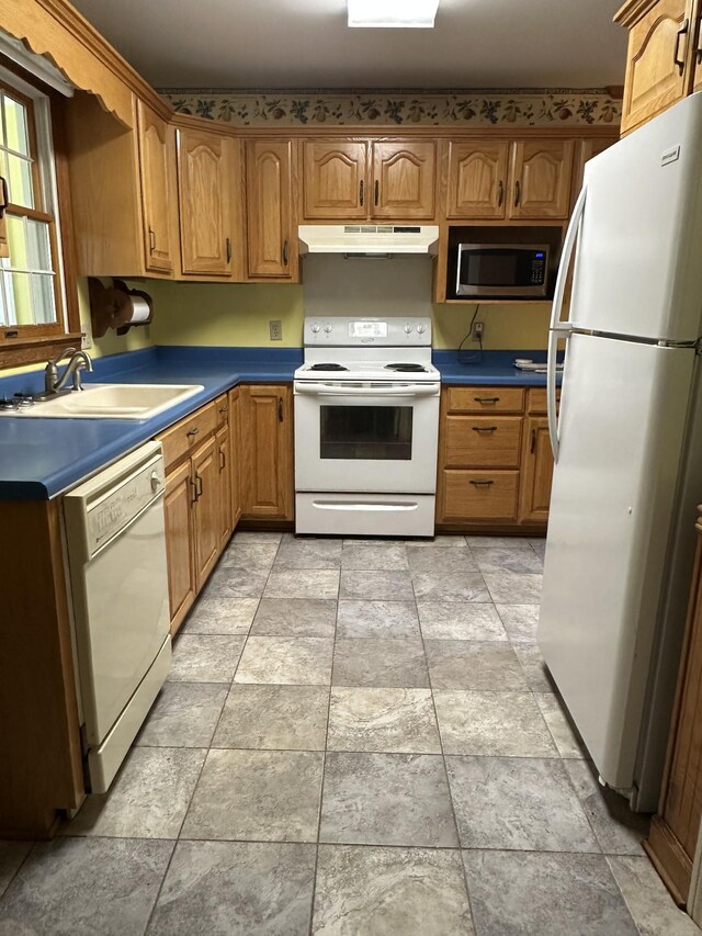 kitchen featuring under cabinet range hood, white appliances, a sink, and stone finish flooring