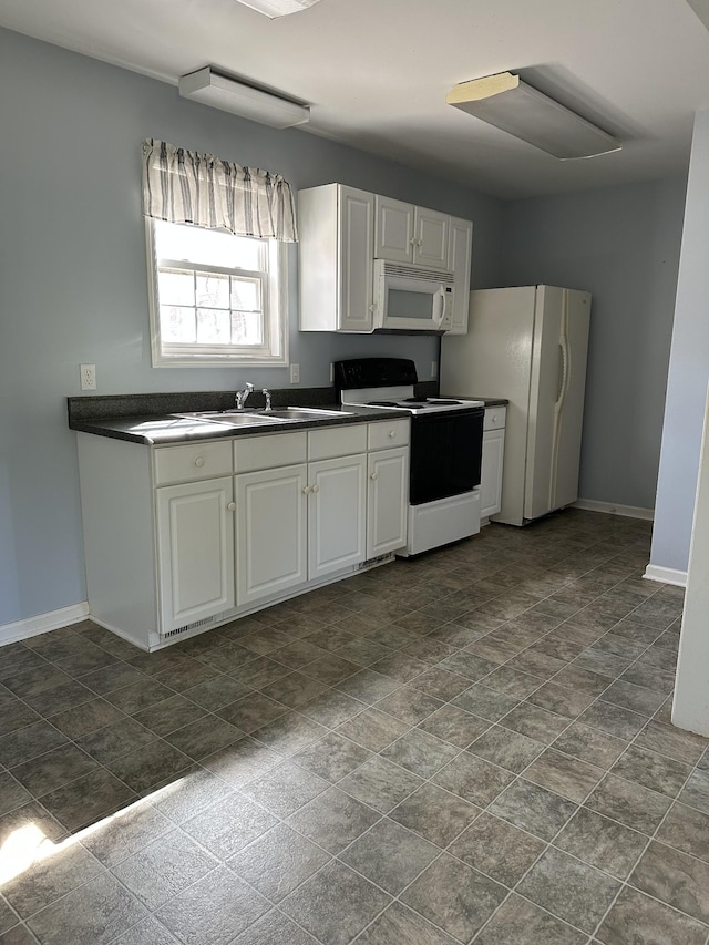 kitchen with a sink, dark countertops, baseboards, white cabinetry, and white appliances