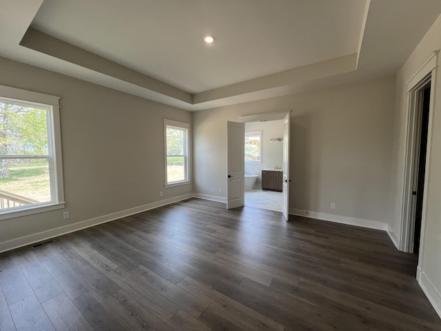 unfurnished bedroom featuring baseboards, visible vents, a tray ceiling, and dark wood-type flooring