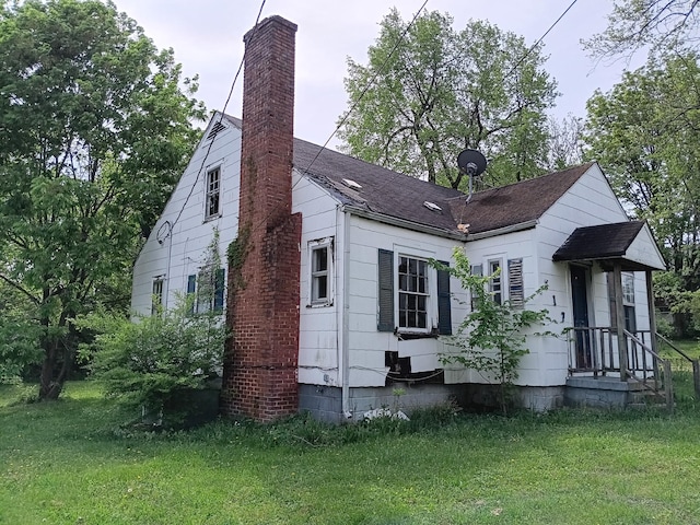rear view of house with a yard, a shingled roof, and a chimney