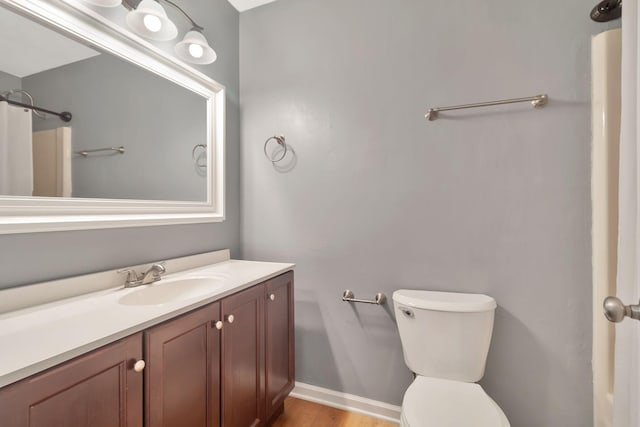 bathroom with baseboards, wood finished floors, toilet, and vanity