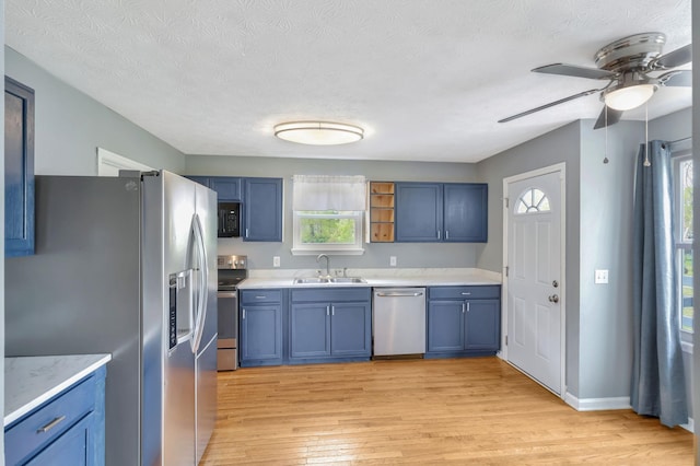 kitchen featuring light wood finished floors, stainless steel appliances, a sink, and ceiling fan