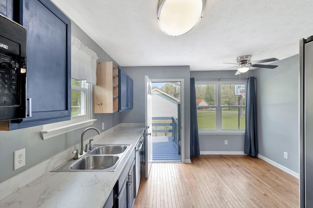 kitchen with a ceiling fan, a sink, light wood-style floors, black microwave, and baseboards