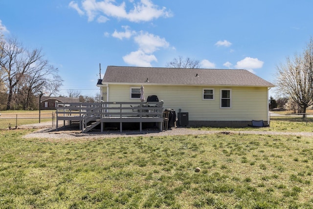 back of house with central air condition unit, fence, a yard, a wooden deck, and roof with shingles