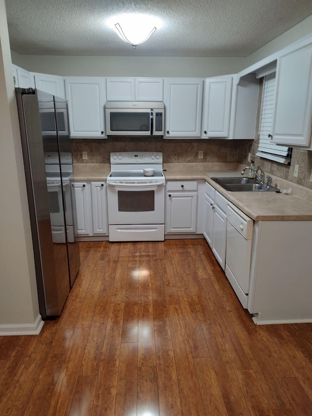 kitchen featuring appliances with stainless steel finishes, light countertops, white cabinets, a sink, and dark wood-type flooring