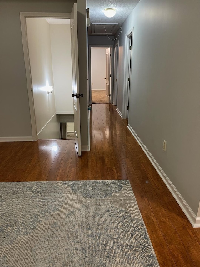 corridor featuring baseboards, hardwood / wood-style flooring, and attic access