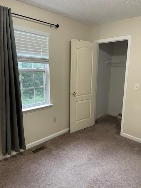 unfurnished bedroom featuring a textured ceiling, visible vents, a closet, baseboards, and carpet floors