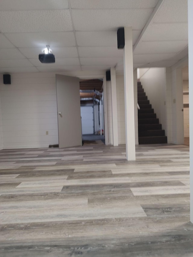 finished below grade area featuring stairs, a drop ceiling, and wood finished floors