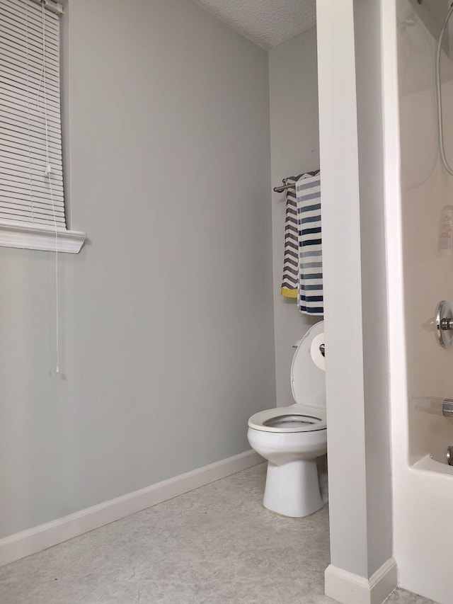 bathroom featuring toilet, a textured ceiling, shower / bathtub combination, and baseboards