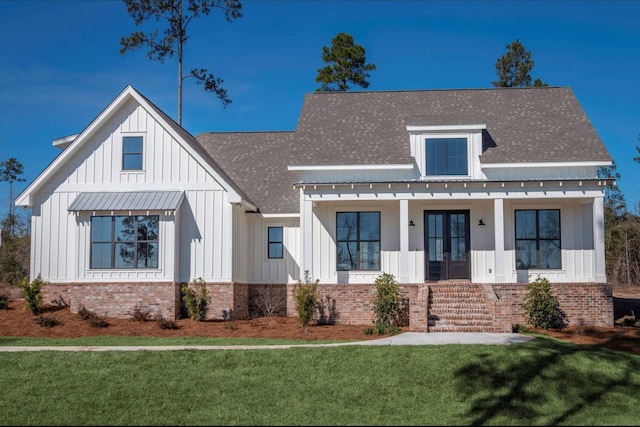 modern farmhouse style home with board and batten siding, a front yard, french doors, and brick siding