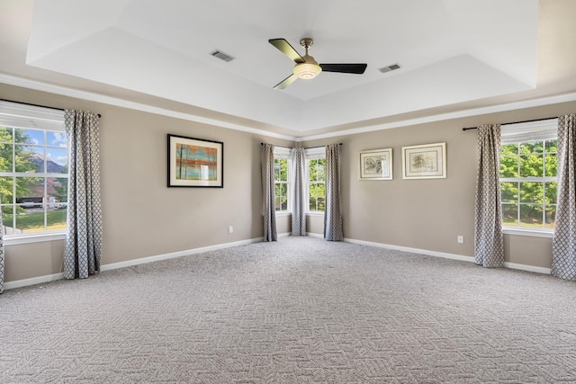 empty room featuring a raised ceiling, ceiling fan, carpet flooring, and visible vents