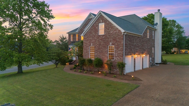 property exterior at dusk with brick siding, a garage, a chimney, concrete driveway, and a lawn