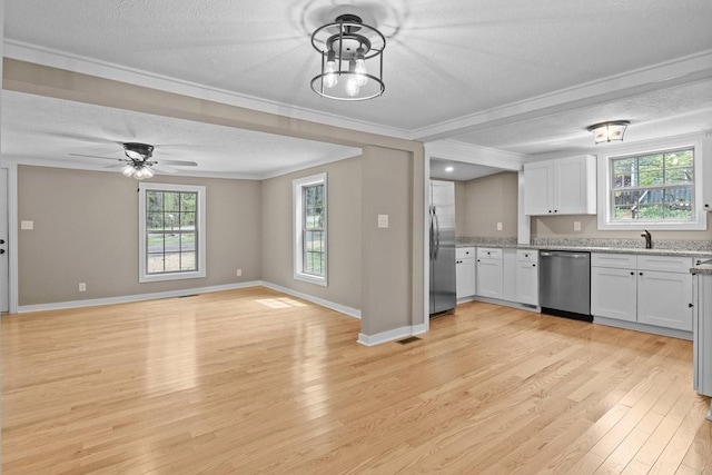 kitchen with light wood finished floors, stainless steel appliances, a textured ceiling, white cabinetry, and crown molding