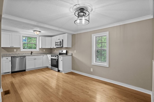 kitchen with light wood finished floors, a textured ceiling, visible vents, crown molding, and appliances with stainless steel finishes