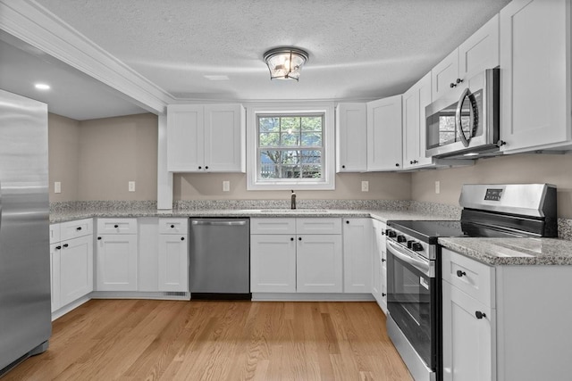 kitchen with light wood finished floors, stainless steel appliances, a sink, and a textured ceiling