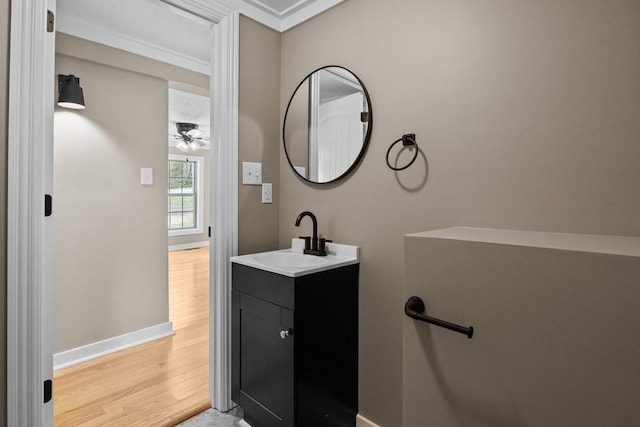 bathroom with wood finished floors, a ceiling fan, vanity, crown molding, and baseboards