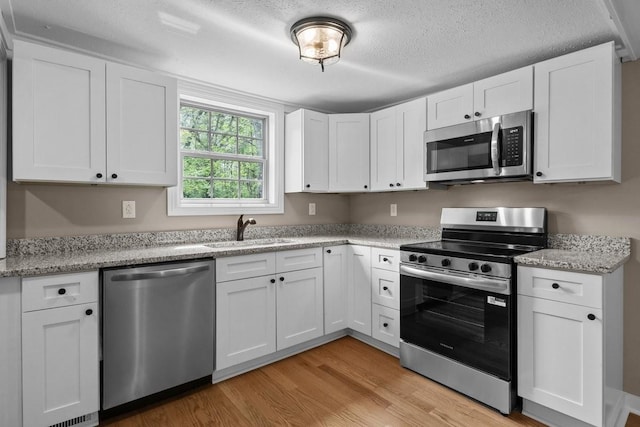 kitchen with white cabinets, stainless steel appliances, light wood-style flooring, a sink, and light stone countertops