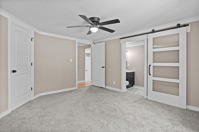 unfurnished bedroom featuring a barn door, a textured ceiling, connected bathroom, ceiling fan, and carpet flooring