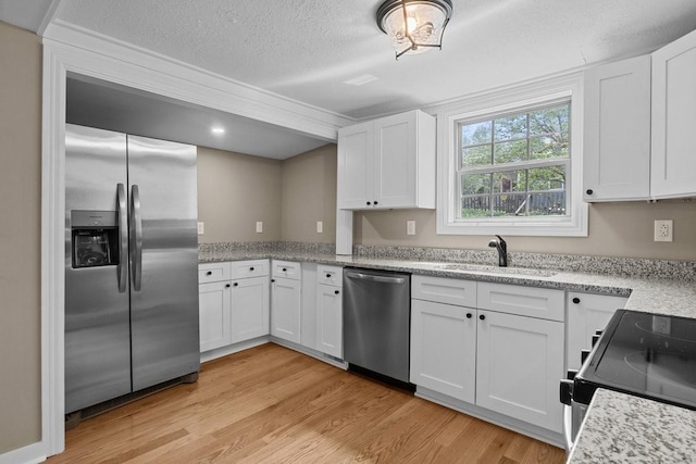 kitchen with white cabinets, light wood finished floors, a sink, a textured ceiling, and appliances with stainless steel finishes