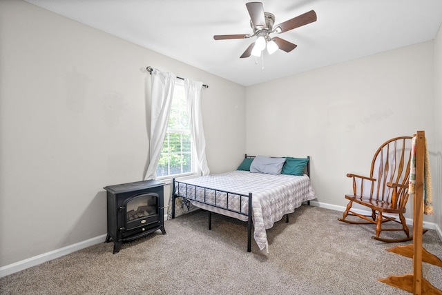 carpeted bedroom featuring baseboards, a ceiling fan, and a wood stove
