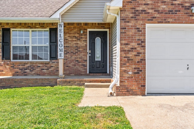 doorway to property with a shingled roof, an attached garage, a lawn, and brick siding