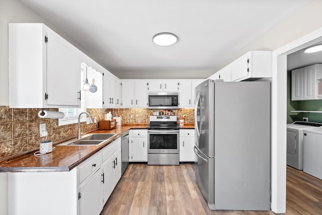 kitchen featuring washer and dryer, dark countertops, light wood-style floors, a sink, and appliances with stainless steel finishes