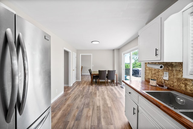 kitchen featuring freestanding refrigerator, baseboards, light wood-type flooring, white cabinetry, and backsplash