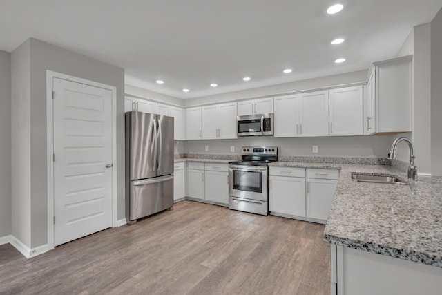kitchen with light wood-style flooring, a sink, white cabinetry, light stone countertops, and appliances with stainless steel finishes