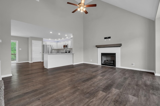 unfurnished living room with baseboards, a brick fireplace, ceiling fan, high vaulted ceiling, and dark wood-type flooring