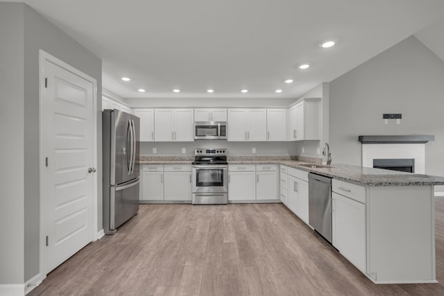 kitchen with white cabinets, stainless steel appliances, light wood-style flooring, and a peninsula