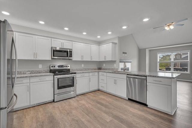 kitchen featuring vaulted ceiling, light wood-style floors, a peninsula, appliances with stainless steel finishes, and white cabinetry