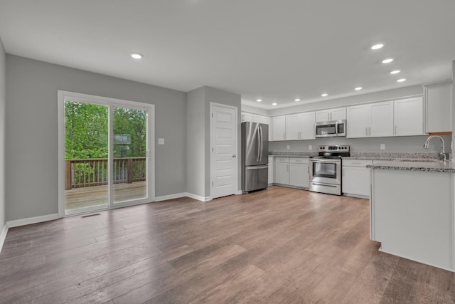 kitchen featuring recessed lighting, light stone counters, stainless steel appliances, and a sink