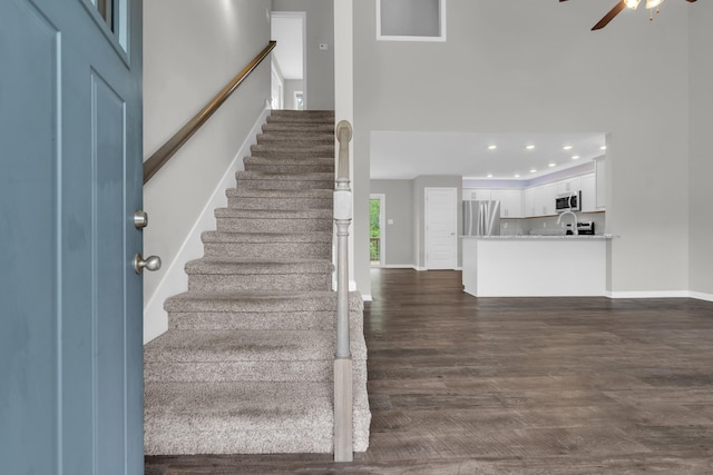 stairs featuring baseboards, wood finished floors, a high ceiling, and ceiling fan