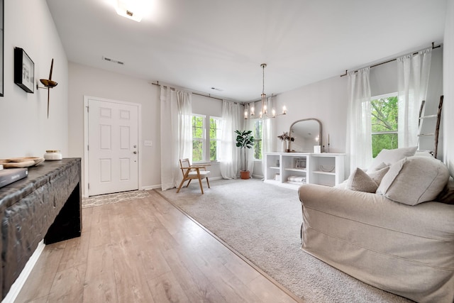 living area with a notable chandelier, light wood finished floors, visible vents, and baseboards