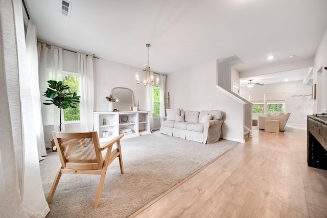 living area featuring visible vents, baseboards, light wood-style flooring, and ceiling fan with notable chandelier