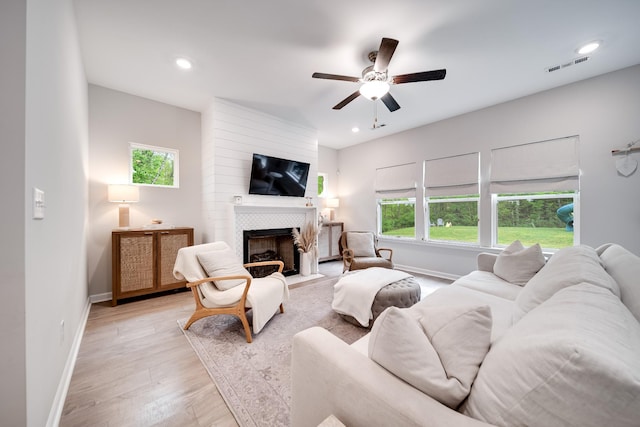 living room with a fireplace, ceiling fan, light wood-type flooring, visible vents, and baseboards