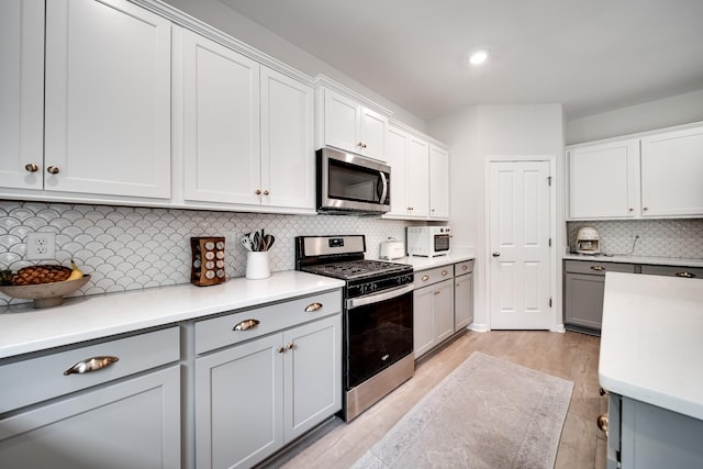 kitchen featuring tasteful backsplash, light wood-style flooring, light countertops, gray cabinetry, and appliances with stainless steel finishes