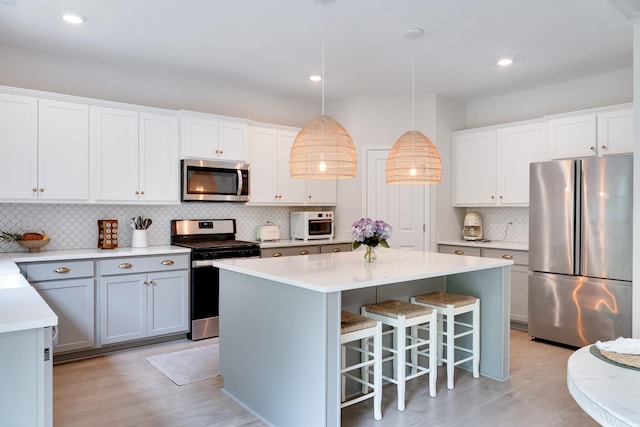 kitchen featuring tasteful backsplash, appliances with stainless steel finishes, light countertops, a center island, and light wood-type flooring