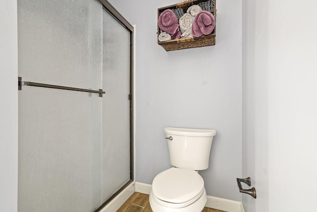 bathroom featuring baseboards, wood finished floors, toilet, and a stall shower