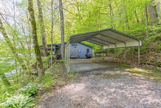 view of car parking featuring dirt driveway, a wooded view, and a detached carport