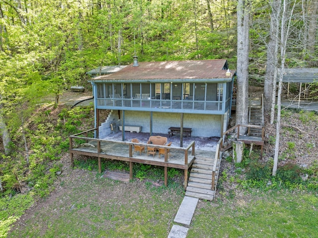 rear view of house with a wooden deck, a forest view, a sunroom, and stairs