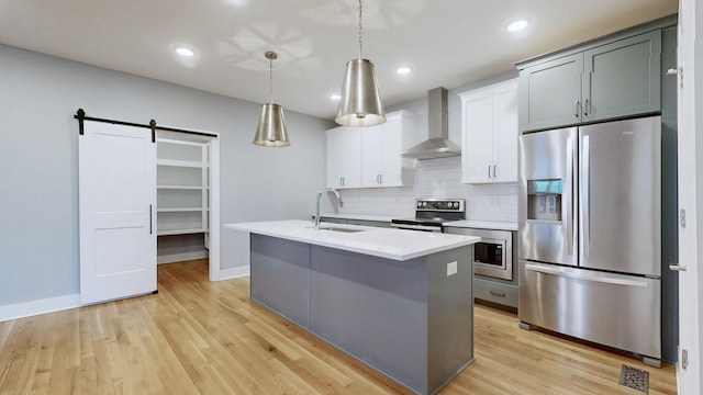 6412B Edsel Dr, Nashville, TN 37209 - kitchen featuring stainless steel appliances, wall chimney range hood, a sink, a barn door, and an island with sink