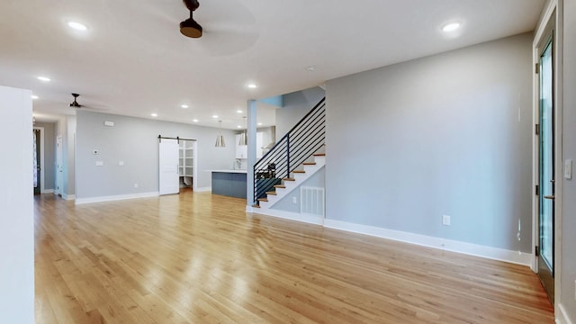 6412B Edsel Dr, Nashville, TN 37209 - unfurnished living room featuring a barn door, a ceiling fan, stairs, light wood-type flooring, and baseboards