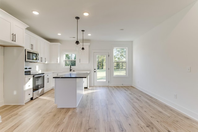 kitchen with light wood finished floors, stainless steel appliances, a sink, white cabinetry, and a kitchen island