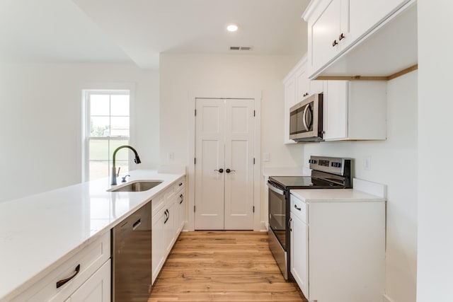 kitchen featuring stainless steel appliances, a sink, light wood-type flooring, white cabinetry, and light countertops