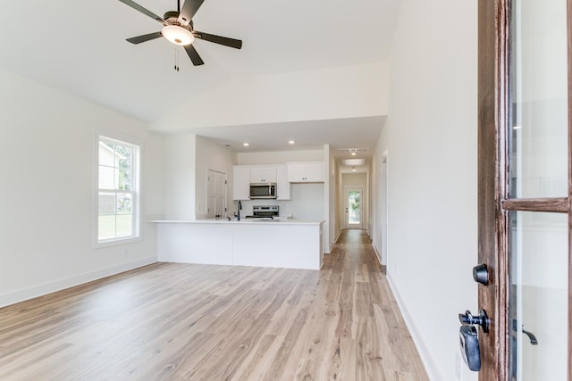 unfurnished living room featuring a ceiling fan, a sink, light wood-style floors, baseboards, and lofted ceiling